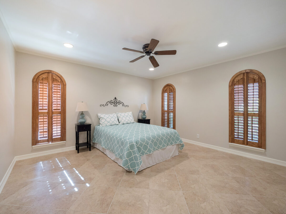 A bedroom with a bed, two windows and a ceiling fan.